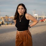 Woman in black crop top and brown pants posing outdoors at sunset.